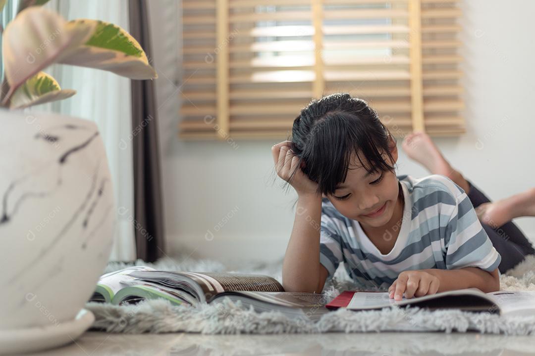 Livro de leitura infantil em casa. Menina deitada e lendo dentro de casa