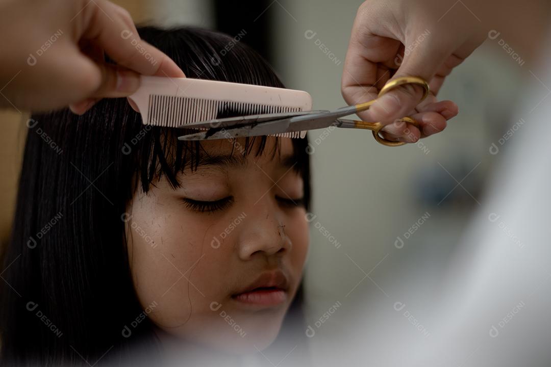 Mãe asiática cortando cabelo para a filha na sala de estar em casa enquanto fica em casa segura do Covid-19 Coronavirus durante o bloqueio. Conceito de auto-quarentena e distanciamento social.