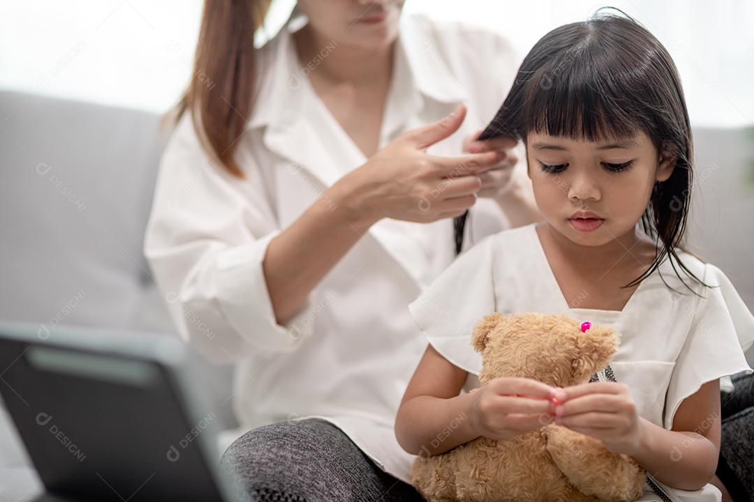 Jovem mãe asiática amarrando o cabelo da filha