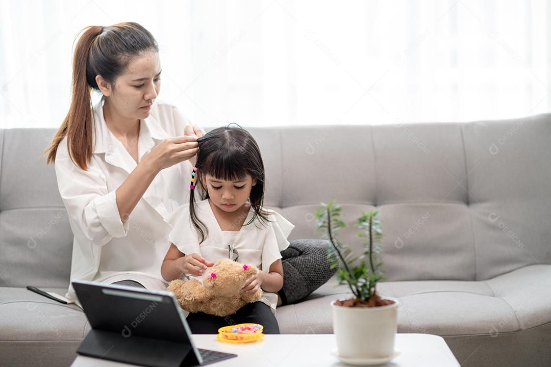 Jovem mãe asiática amarrando o cabelo da filha