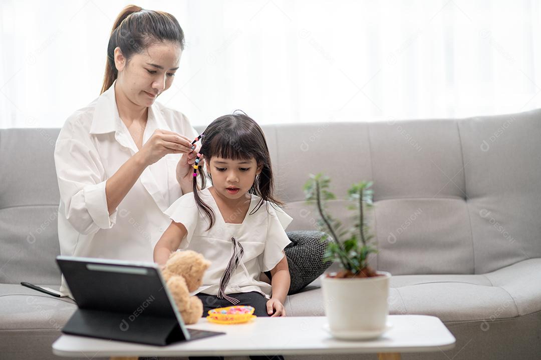 Jovem mãe asiática amarrando o cabelo da filha