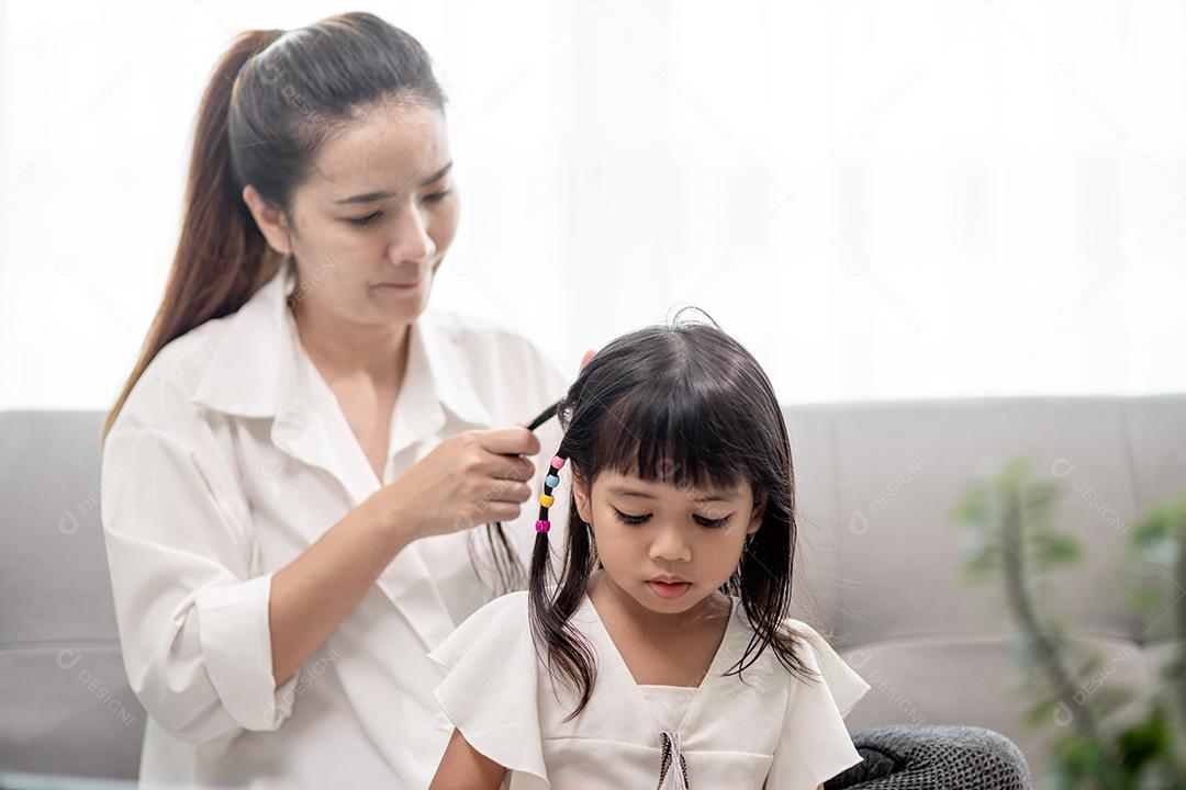 Jovem mãe asiática amarrando o cabelo da filha