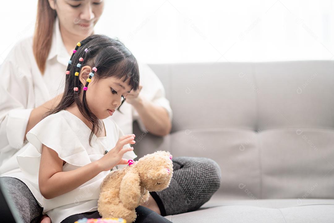 Jovem mãe asiática amarrando o cabelo da filha