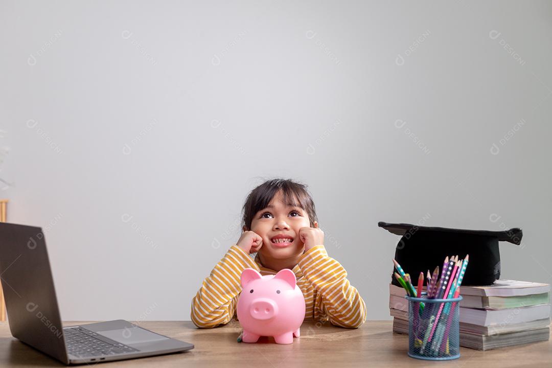 Menina asiática usando um chapéu de formatura com um cofrinho rosa, economizando dinheiro, investindo no futuro,