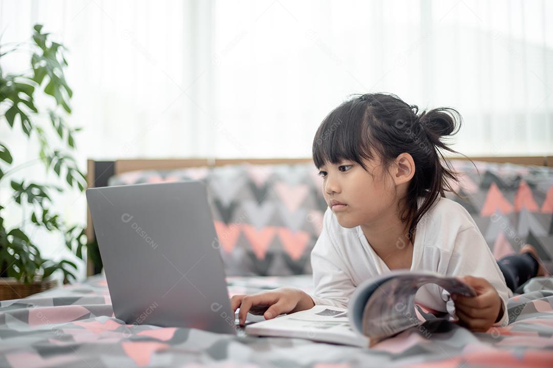 Menina asiática usando um laptop enquanto estava deitado na cama