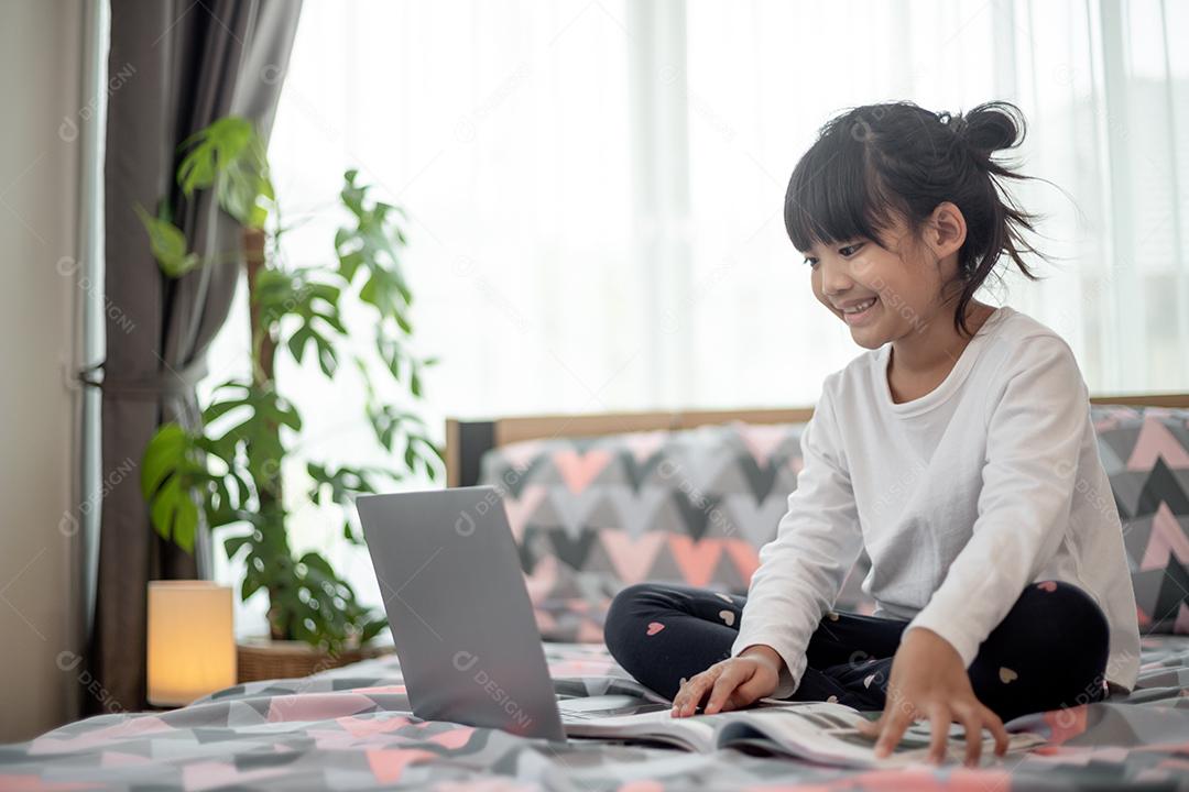 Menina asiática usando um laptop enquanto estava deitado na cama