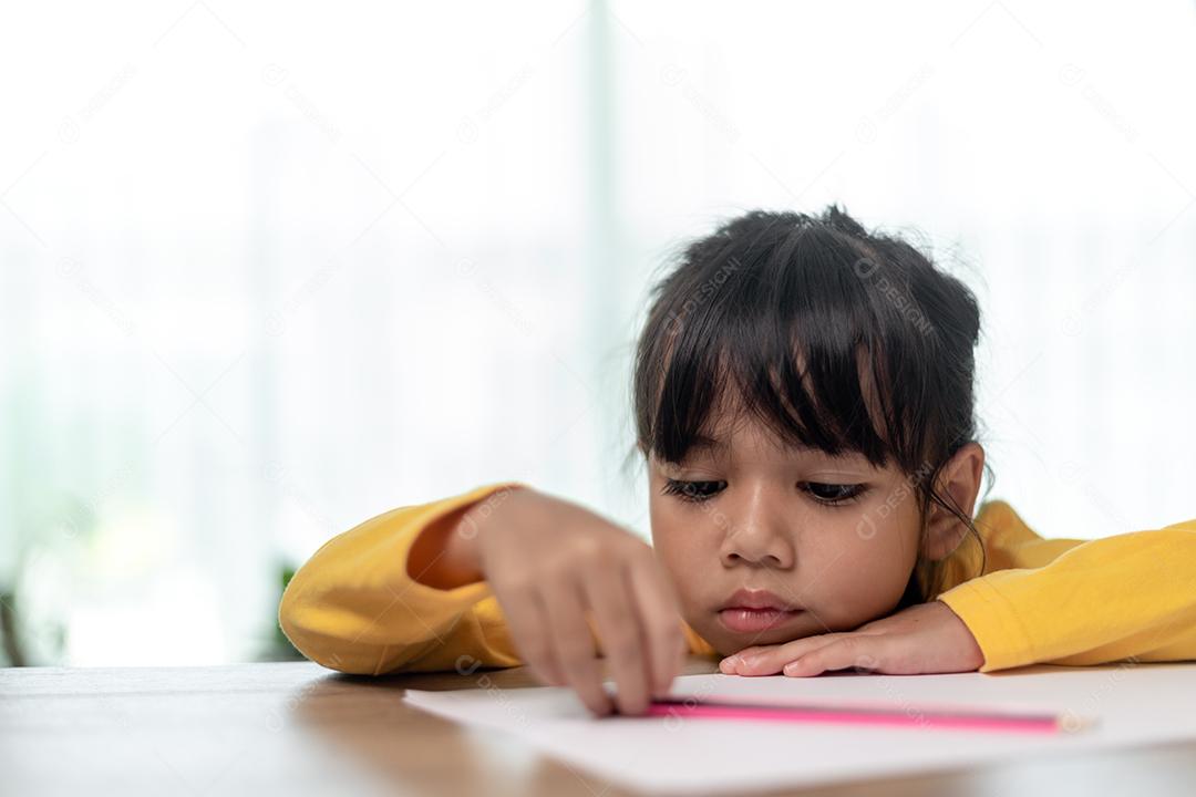 Menina asiática sentada sozinha e olhando com um rosto entediado, criança pré-escolar deitada de cabeça na mesa com triste entediado com lição de casa, criança mimada