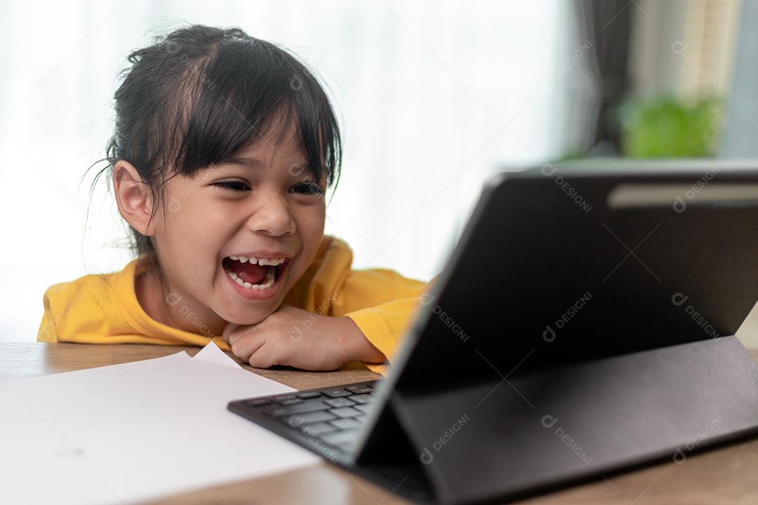Menina asiática tendo aula on-line e feliz pelo conceito de pandemia de coranavírus de quarentena escolar em casa