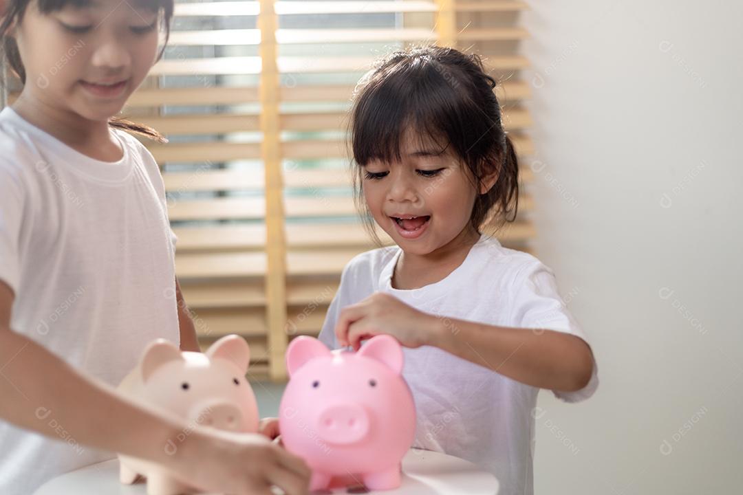 Menina asiática economizando dinheiro em um cofrinho, aprendendo sobre economia, Kid economiza dinheiro para educação futura. Conceito de dinheiro, finanças, seguros e pessoas