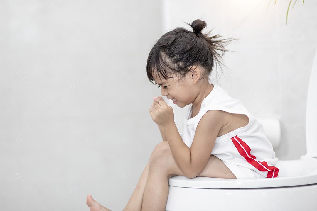 A garotinha está sentada no vaso sanitário sofrendo de constipação ou hemorroida.