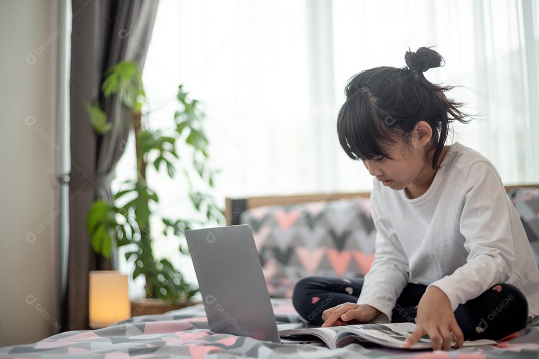 Menina asiática usando um laptop enquanto estava deitado na cama