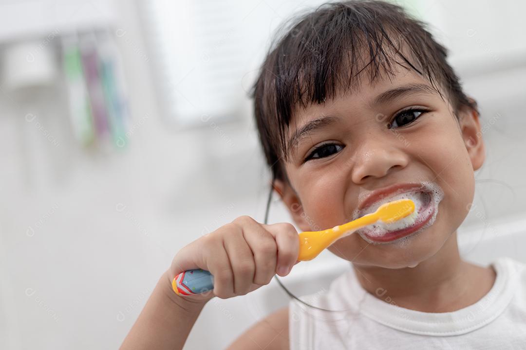 Menina bonitinha limpando os dentes com uma escova de dentes no banheiro