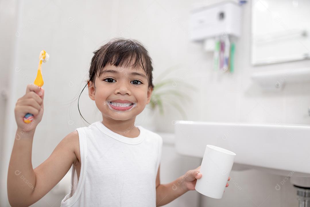 Menina bonitinha limpando os dentes com uma escova de dentes no banheiro