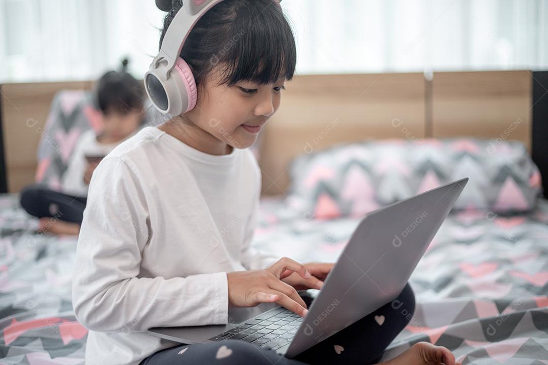 Menina asiática usando um laptop enquanto estava deitado na cama