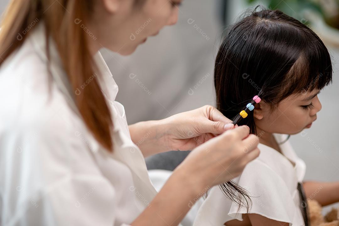 Jovem mãe asiática amarrando o cabelo da filha