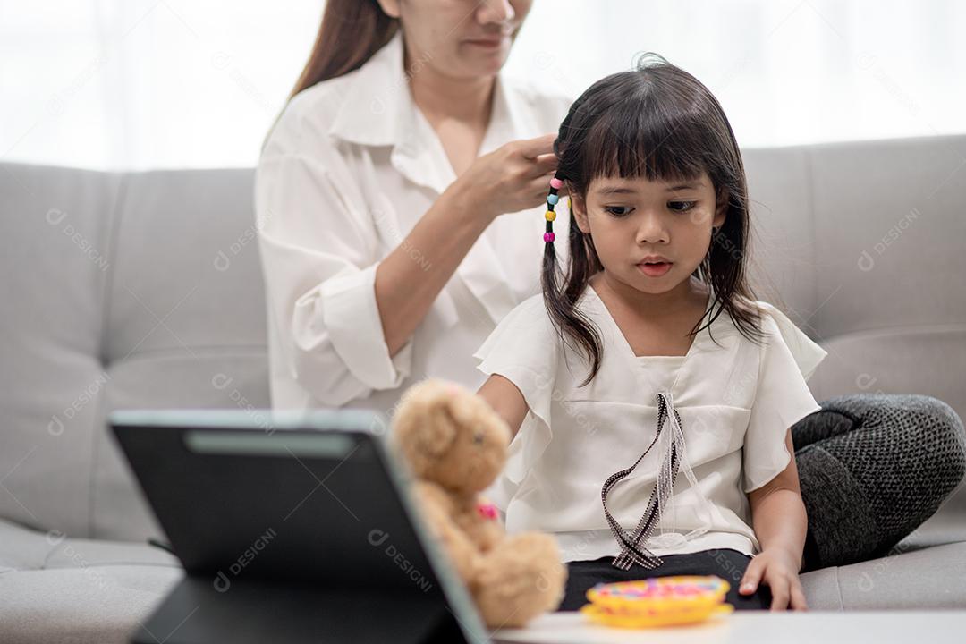 Jovem mãe asiática amarrando o cabelo da filha