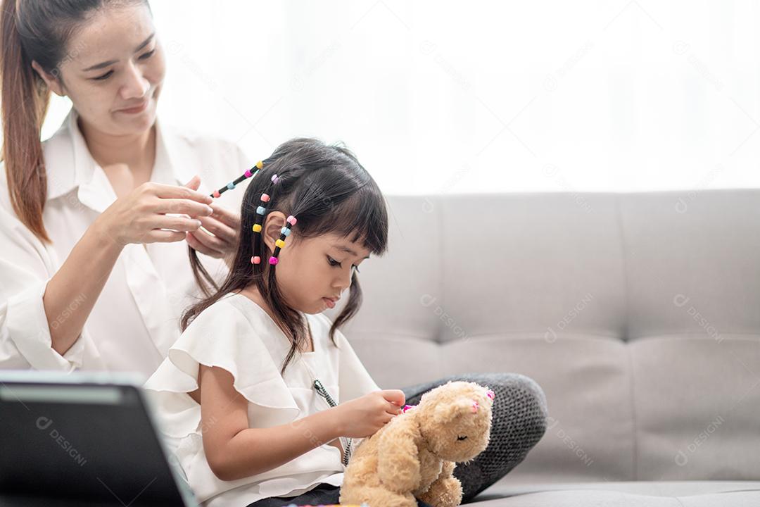 Jovem mãe asiática amarrando o cabelo da filha