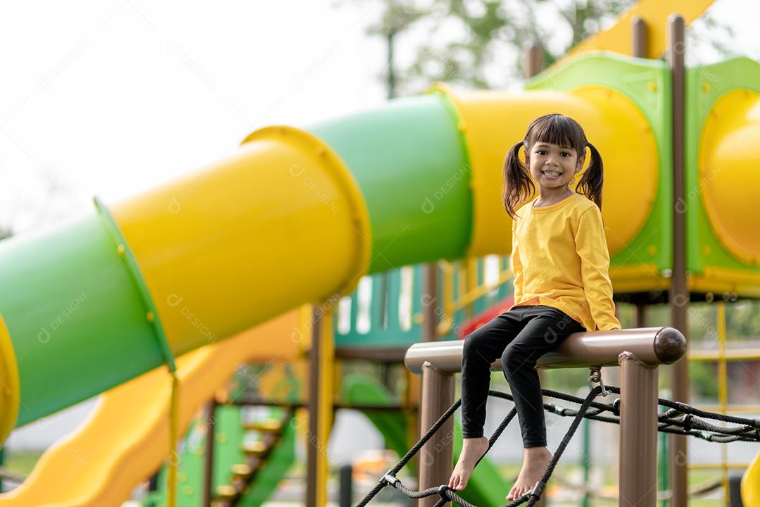 Menina asiática brincando no playground no parque ao ar livre Momento feliz e boa emoção