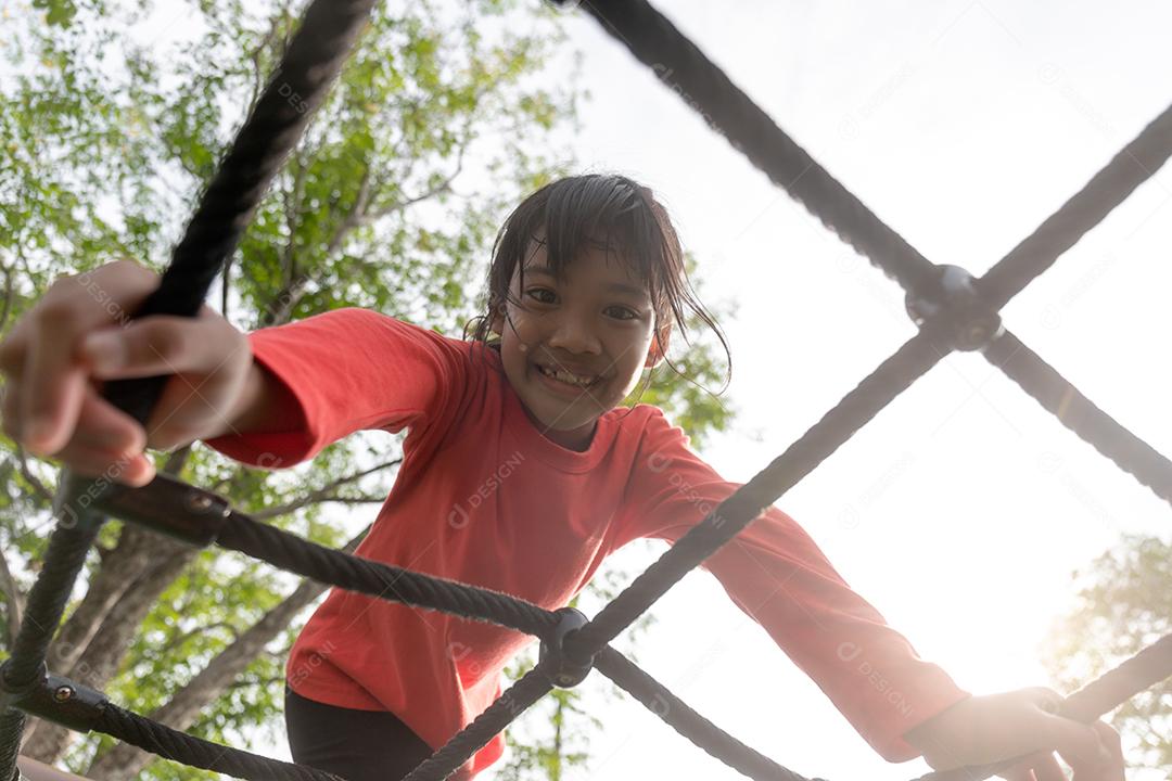 conceito de verão, infância, lazer e pessoas - menina feliz no quadro de escalada do parque infantil