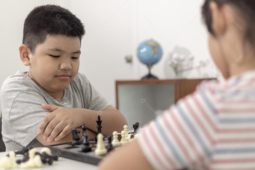 Menino e menina estão jogando xadrez em casa. Crianças jogando xadrez