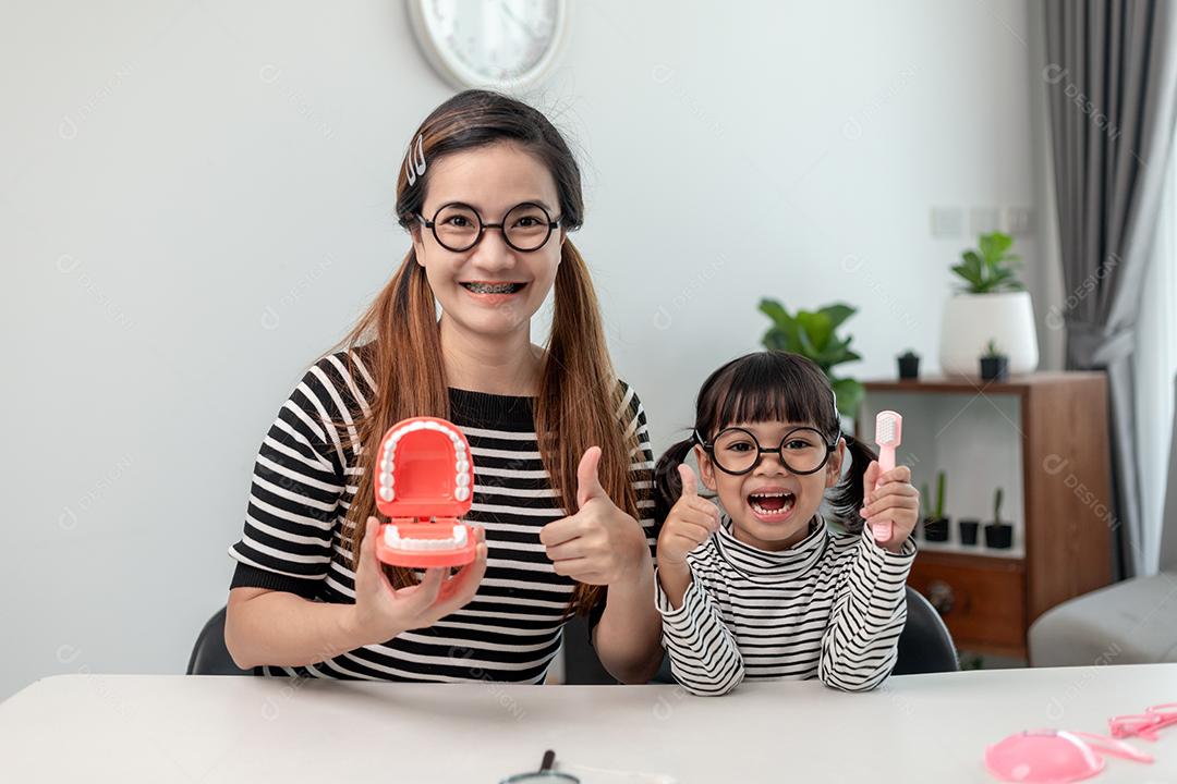 mãe ensinando filha criança escovando os dentes em casa