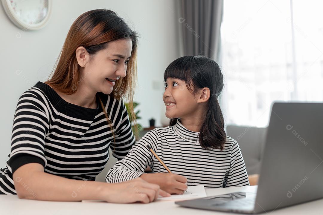 Garotinha asiática aprendendo aula online em casa com mãe