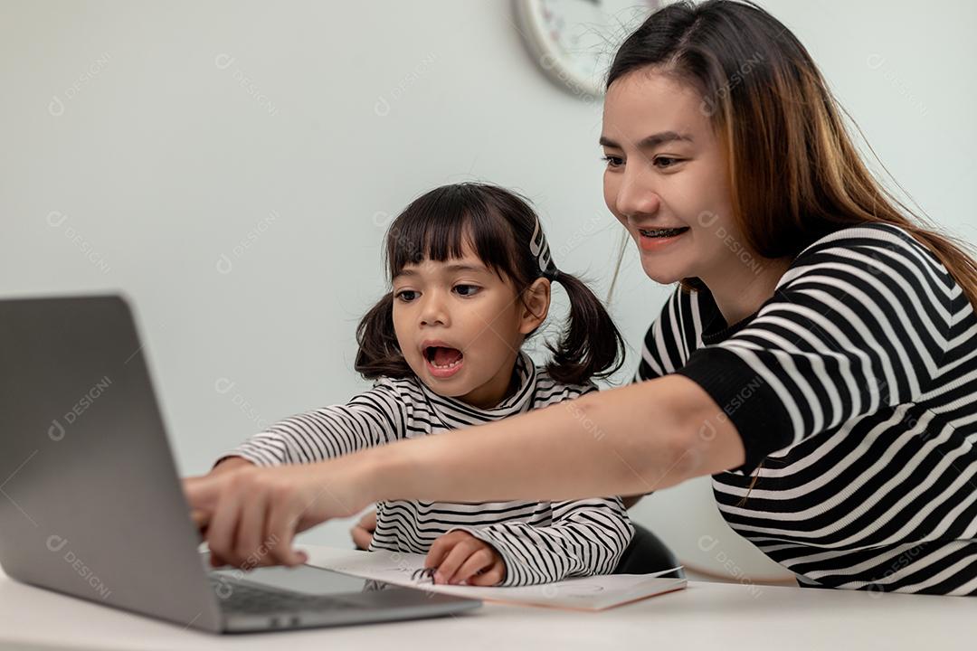 Garotinha asiática aprendendo aula online em casa com mãe