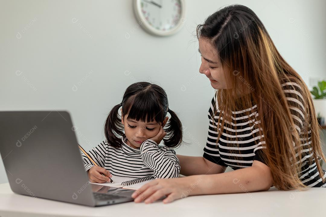 Garotinha asiática aprendendo aula online em casa com mãe