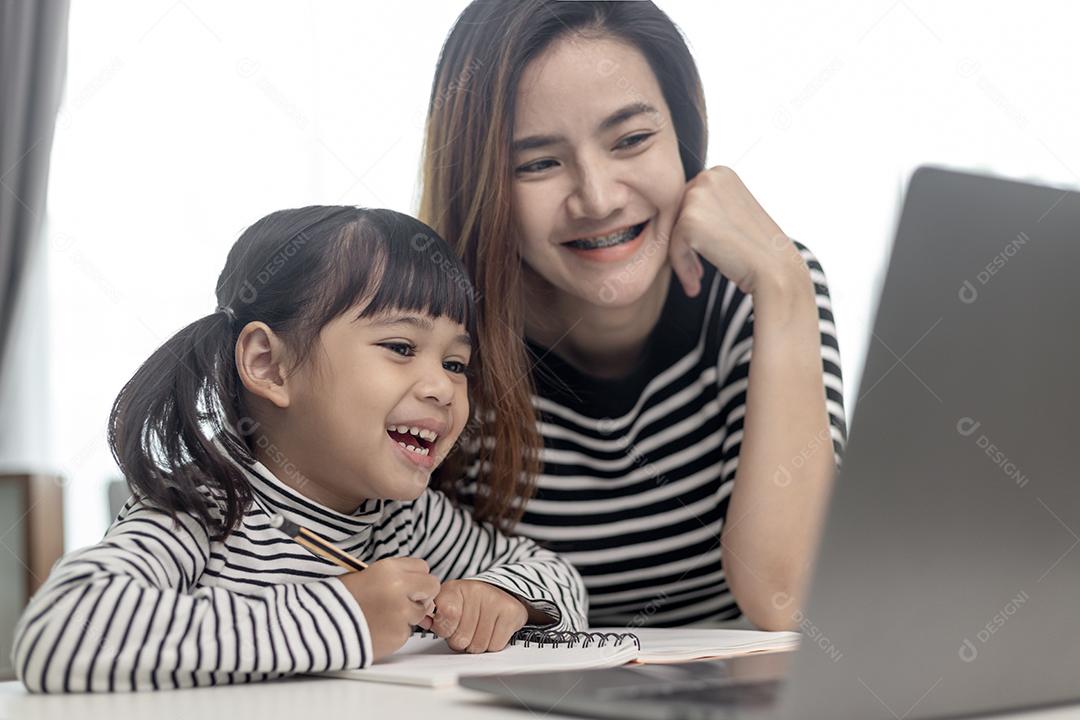 Garotinha asiática aprendendo aula online em casa com mãe