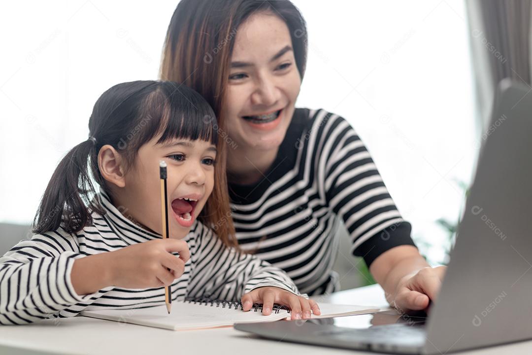 Garotinha asiática aprendendo aula online em casa com mãe