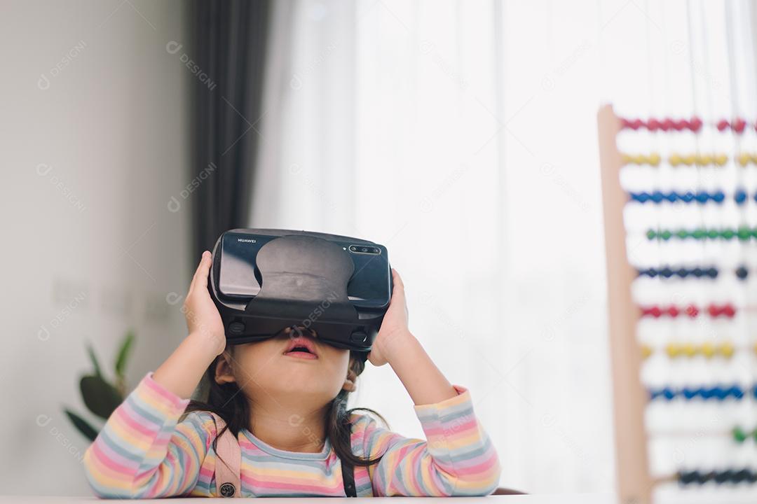 Criança com fone de ouvido de realidade virtual sentado atrás da mesa dentro de casa