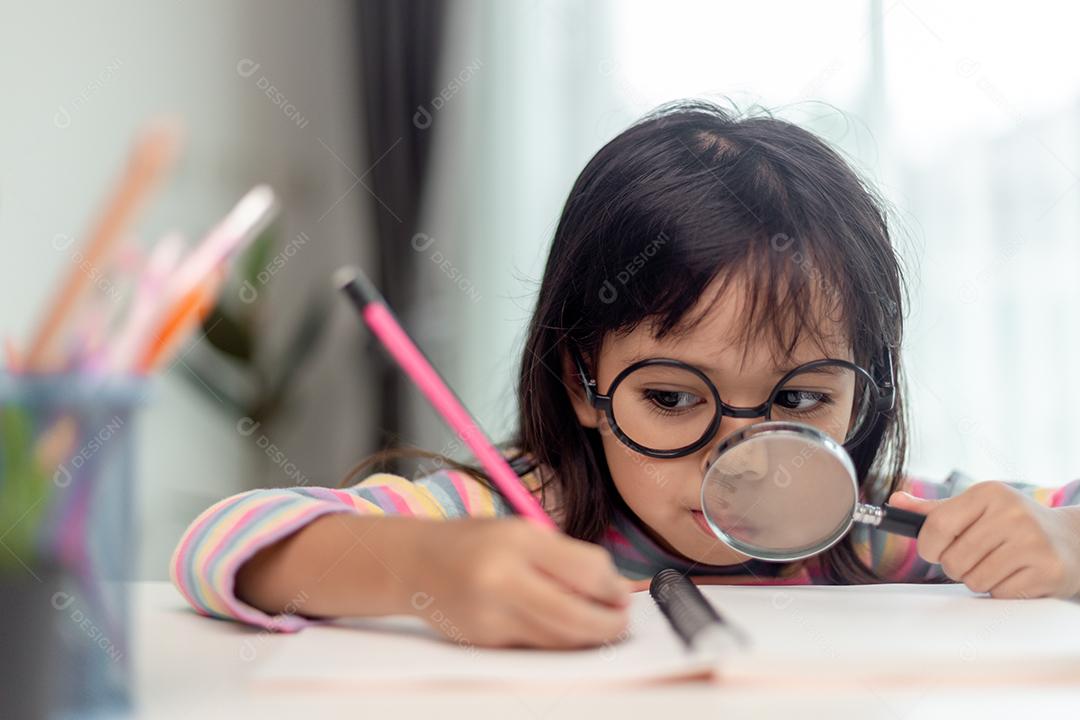 Estudante menina asiática escrevendo com uma lupa olhando