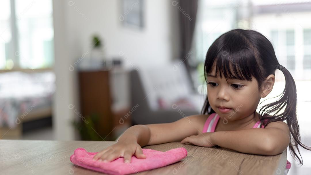 menina asiática feliz aprendendo a limpar com um pano no livi