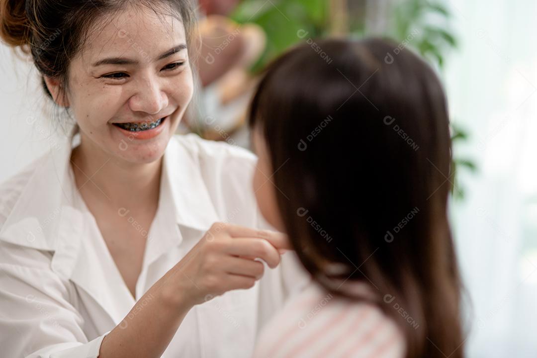 Mãe asiática cortando cabelo para sua filha na sala de estar em casa