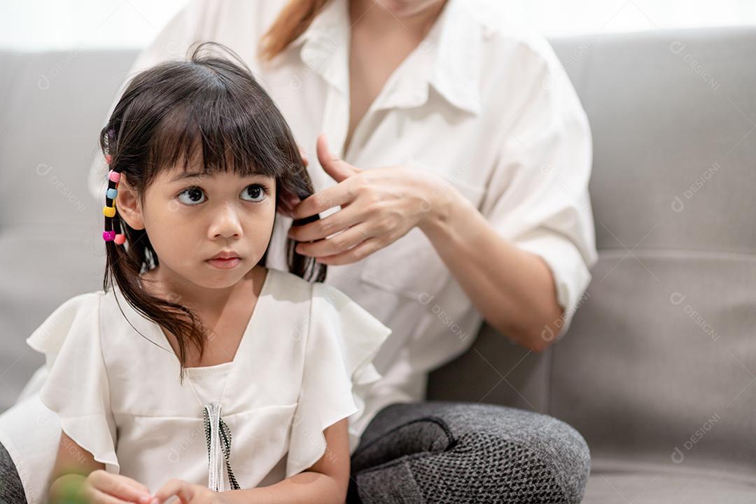 Young Asian mother tying her daughter's hair