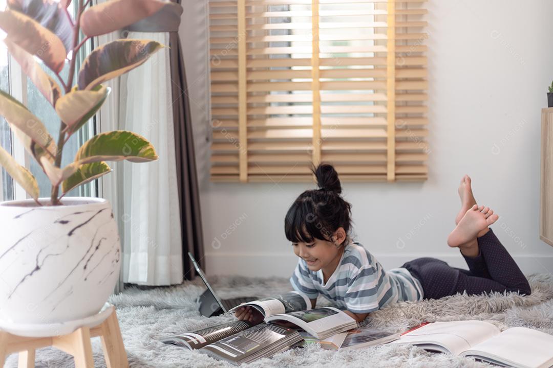 Livro de leitura infantil em casa. Menina deitada e lendo dentro de casa