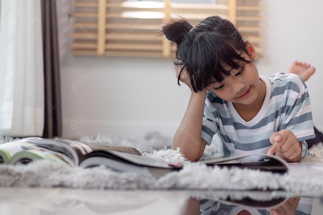 Livro de leitura infantil em casa. Menina deitada e lendo dentro de casa