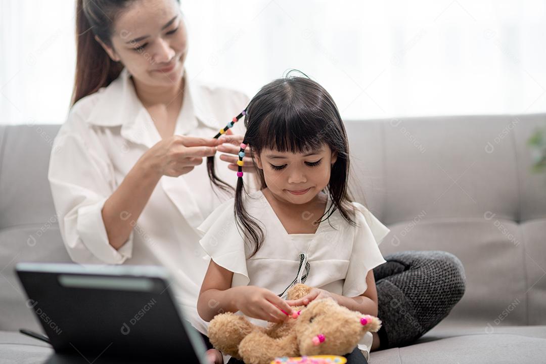 Jovem mãe asiática amarrando o cabelo da filha