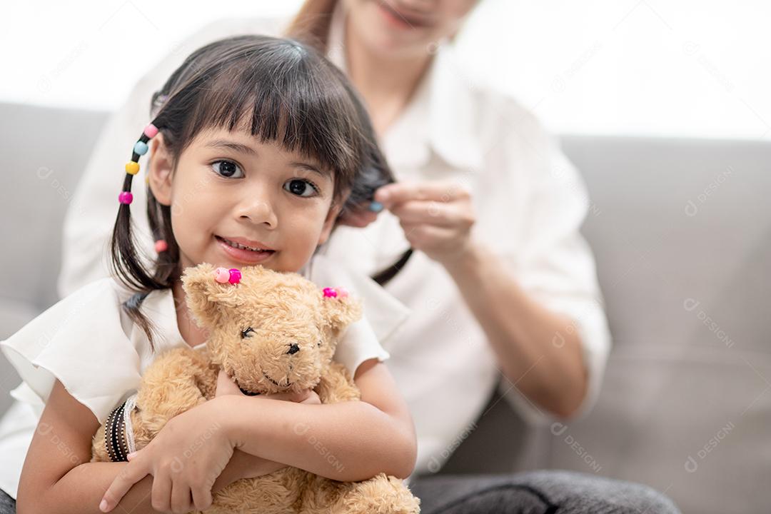Jovem mãe asiática amarrando o cabelo da filha