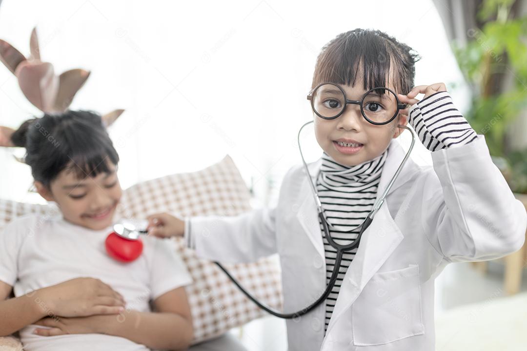 Duas crianças bonitas brincam de médico e hospital usando estetoscópio. Meninas de amigos se divertindo em casa ou pré-escola.