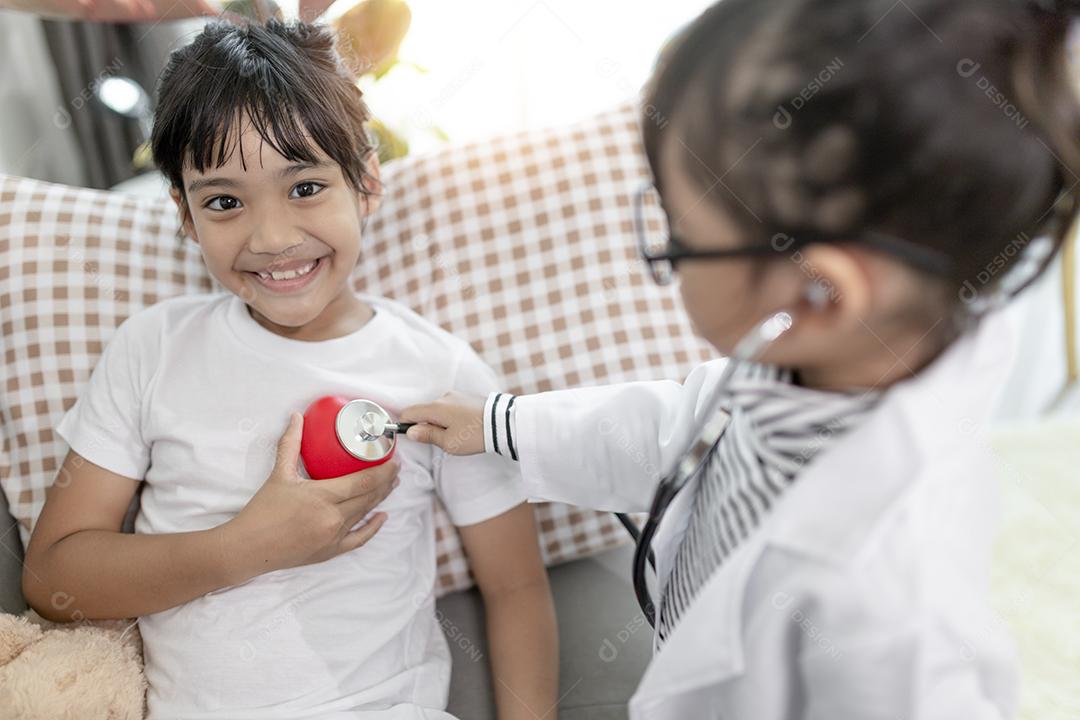 Duas crianças bonitas brincam de médico e hospital usando estetoscópio. Meninas de amigos se divertindo em casa ou pré-escola.