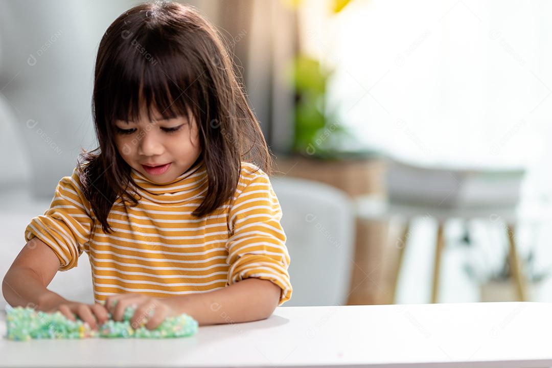 A garotinha está aprendendo a usar massinha colorida em uma sala bem iluminada