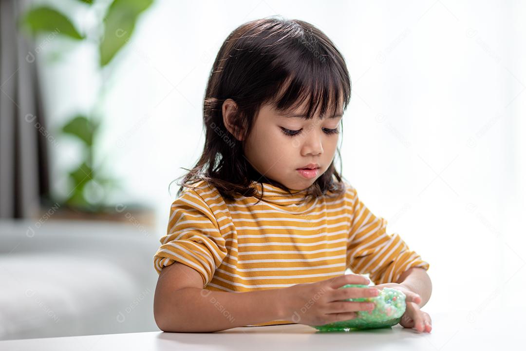 A garotinha está aprendendo a usar massinha colorida em uma sala bem iluminada