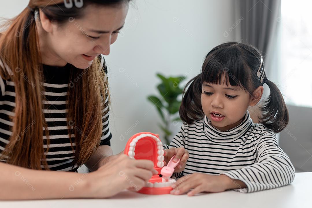 mãe ensinando filha criança escovando os dentes em casa