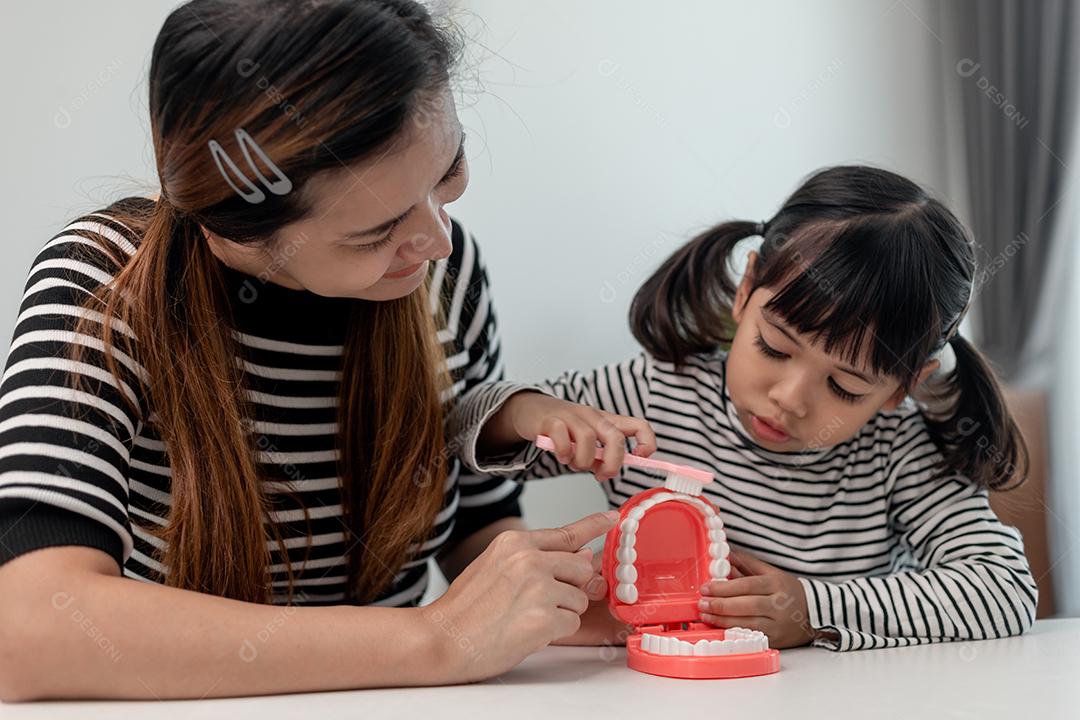 mãe ensinando filha criança escovando os dentes em casa