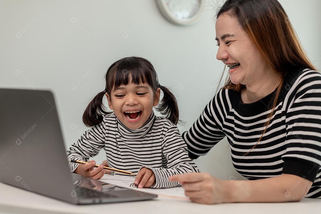 Asian little girl learning online class at home with her mother. Preschool child use laptop to do homework, school teacher home schooling by digital remote internet with mother support.