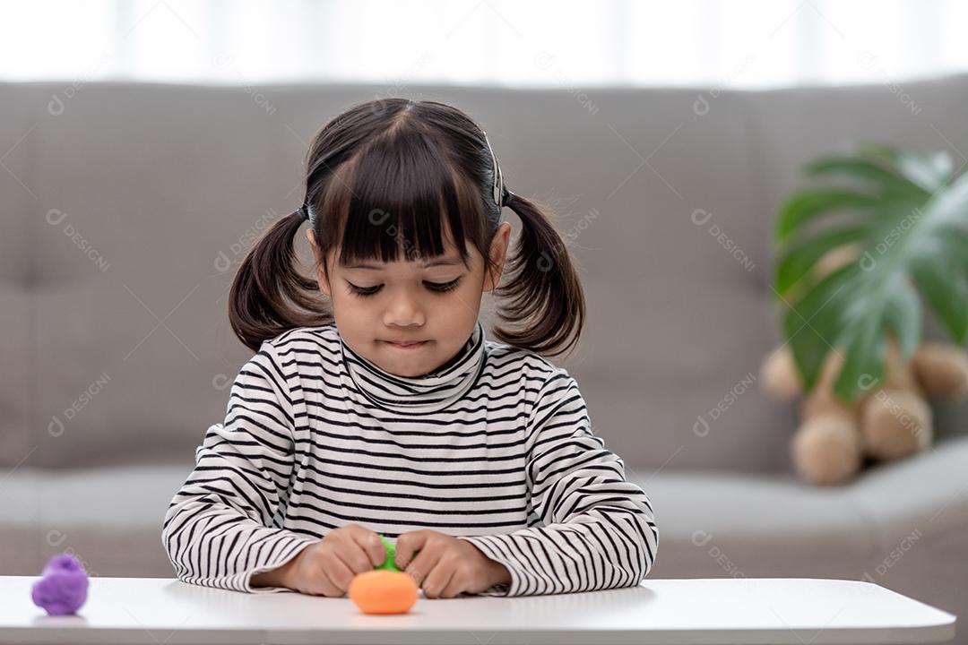 A garotinha está aprendendo a usar massinha colorida em uma sala bem iluminada