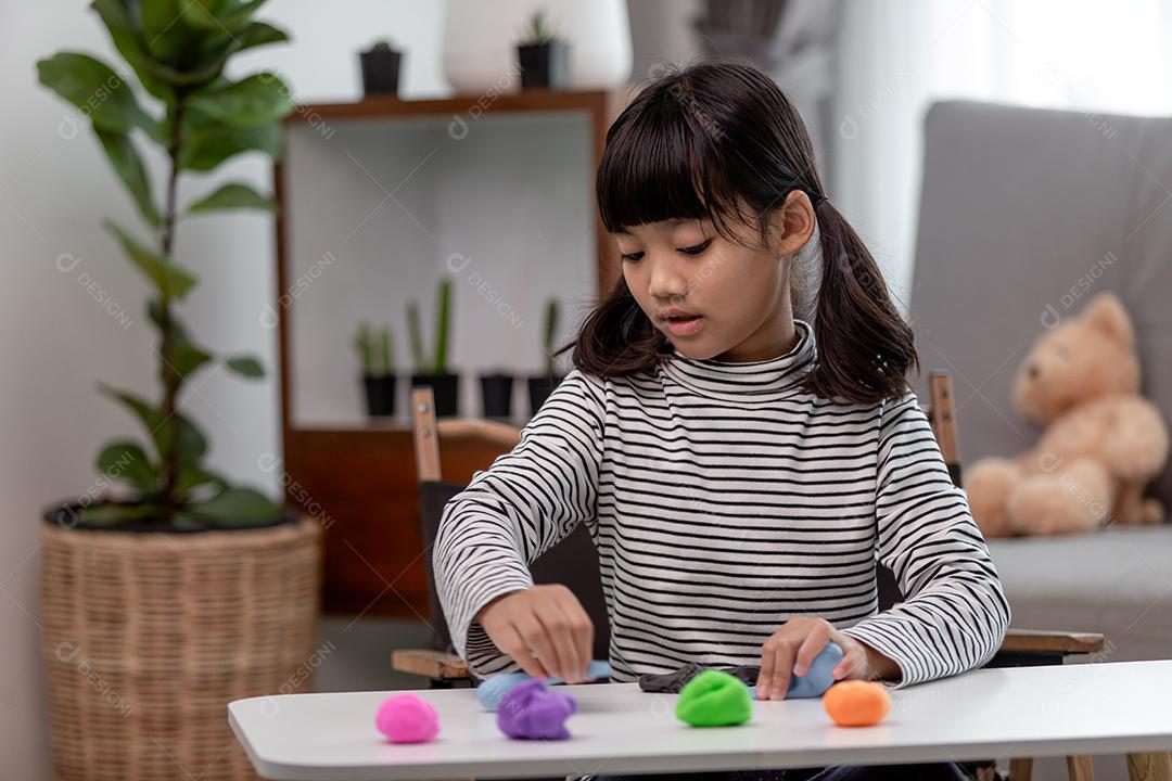 A garotinha está aprendendo a usar massinha colorida em uma sala bem iluminada