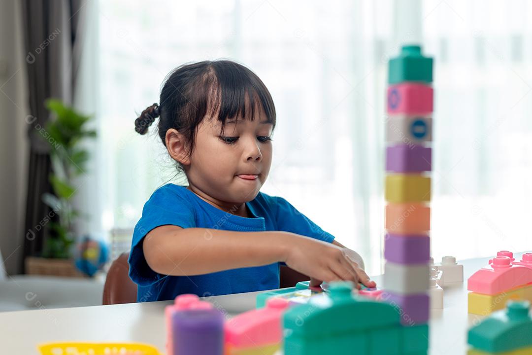 Adorável menina jogando blocos de brinquedo em uma sala iluminada
