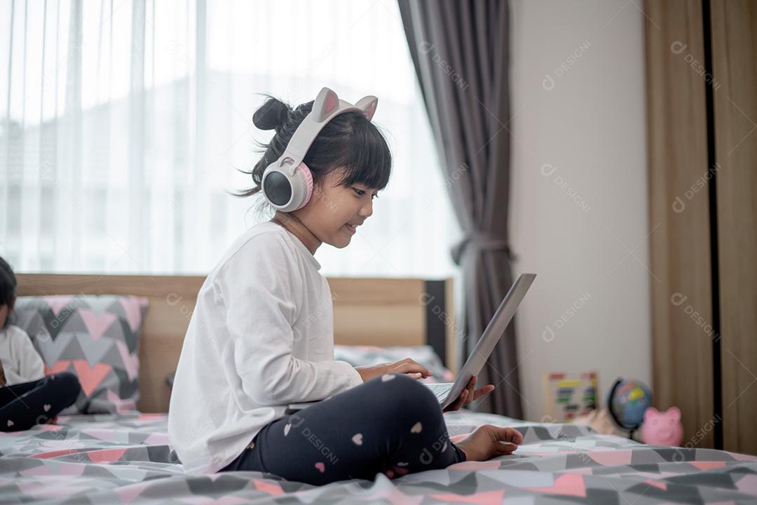 Menina asiática usando um laptop enquanto estava deitado na cama